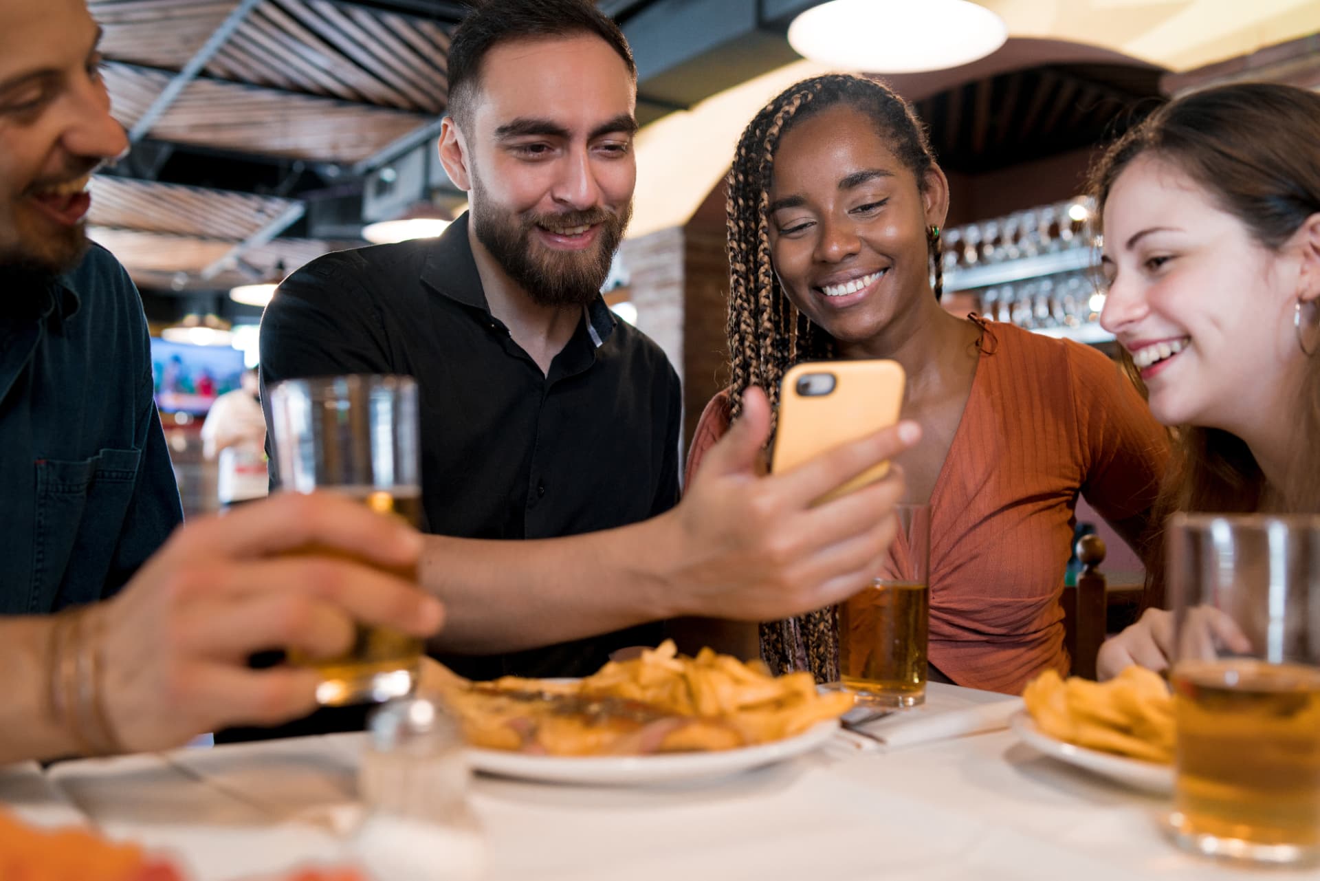 Friends laughing together around a restaurant table with beers and fries